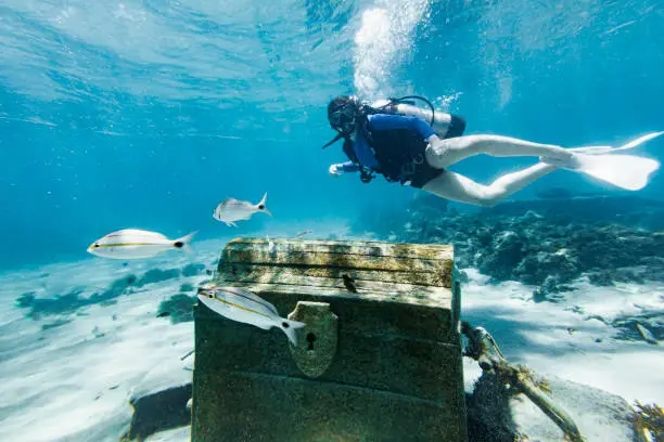 Teenage girl scuba diving over a pirate chest on the bottom of the sea