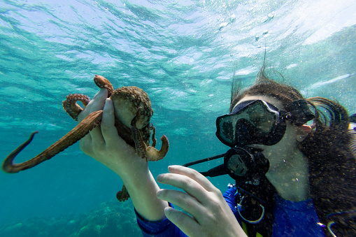 Teenage girl holding a octopus in her hand under the sea.