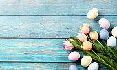 Easter background with eggs and tulips on blue wooden backdrop, top view flat lay