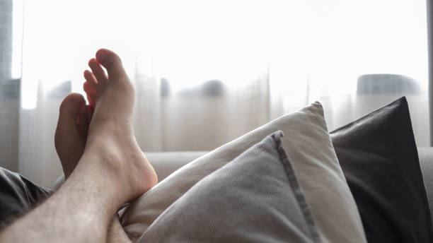 Man stretching legs in mosquito net on the bed at vacation, Sunlight through white curtain in bedroom