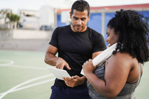 istock Curvy woman talking with her personal trainer while checking tech clipboard outdoor - Focus on trainer 1373099529