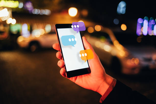 Female hand holding smartphone with chat box icons pop up on night city street, close-up. Concept chatting conversation, online service, social media interactions