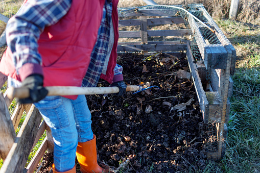 Young African woman is turning a pile of compost with pitchfork.