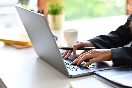 Close-up image of a businesswoman's hand typing on a computer laptop at the white working desk.