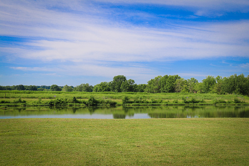 a rural lake green grass wild nature preserve park grassland pond reflection blue sky cloudscape