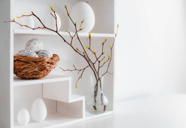 istock Home minimalist interior with Easter decor. Branches with budding buds in a glass vase on shelves in the shape of a house, 1373117016