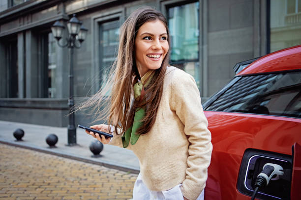 porträt einer frau, die ihr elektroauto auflädt - netzstecker stock-fotos und bilder