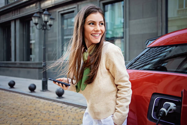 portrait of woman charging her electric car - electric car imagens e fotografias de stock