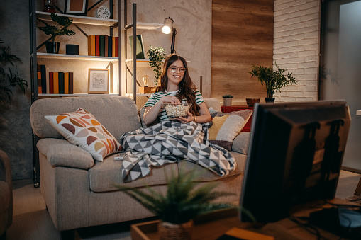 Woman watching tv in the night sitting on a couch in the living room at home