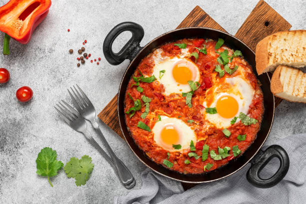 istock Shakshuka in a frying pan on a gray rustic background. Jewish scrambled eggs. Poached eggs in a spicy tomato pepper sauce. Top view, flat lay. 1373126785