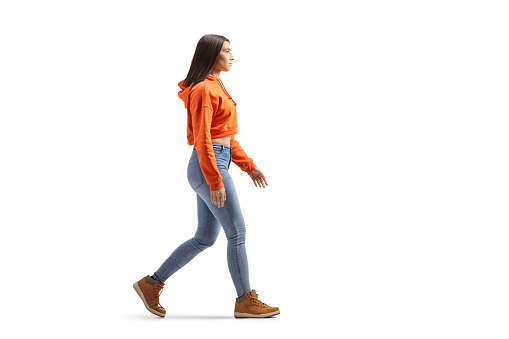 Full length profile shot of a young female in jeans and sweatshirt walking isolated on white background