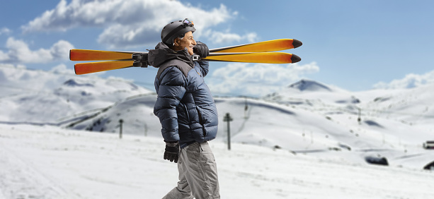 Mature man in a winter jacket walking and carrying skiis on a snowy mountain