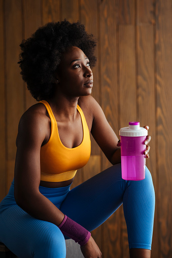 Young athletic woman sitting in fitness studio with bottle of water