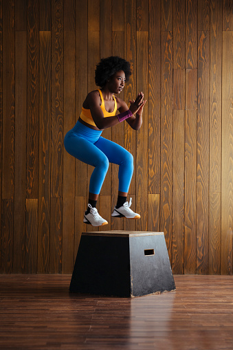 Young fit woman jumping on wooden platform as part of workout