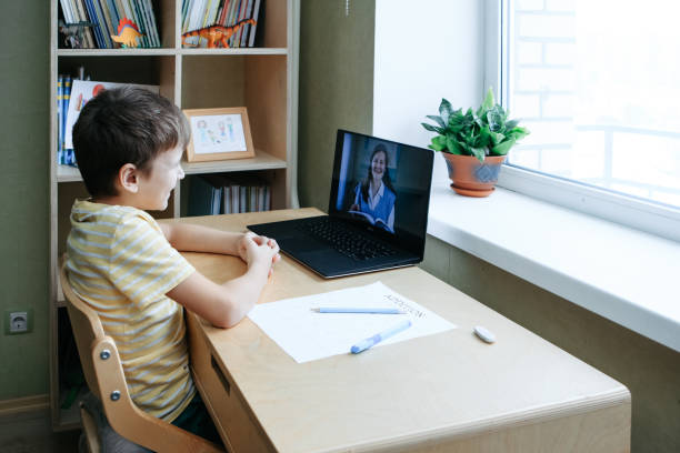 istock 8 years old boy sit by desk with laptop and do writing task during online lesson 1373130931