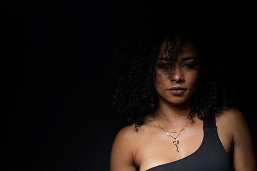 Latin woman of average age from 20 to 29 years of age with Afro hair and skin is dressed all in black with a black background and is photographed in portraits