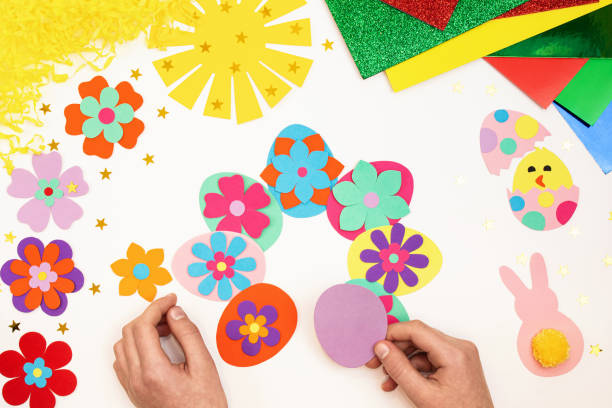 istock Composition of Easter eggs, wreath, flowers, sun, chicken, rabbit from multi-colored paper, step by step. Child makes crafts his own hands. Easter DIY handmade art creativity. Top view, copy space 1373133059