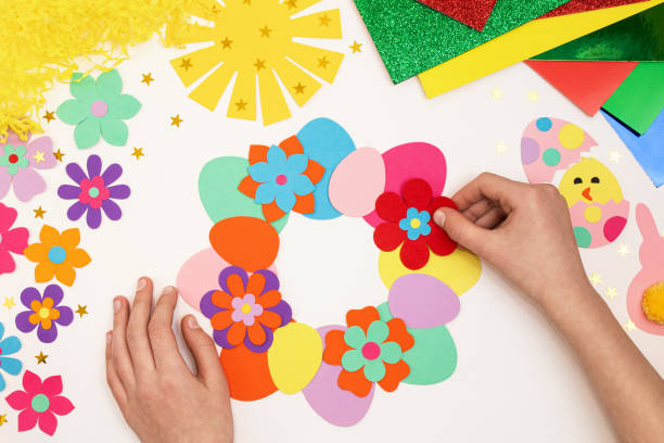 istock Composition of Easter eggs, wreath, flowers, sun, chicken, rabbit from multi-colored paper, step by step. Child makes crafts his own hands. Easter DIY handmade art creativity. Top view, copy space 1373133068
