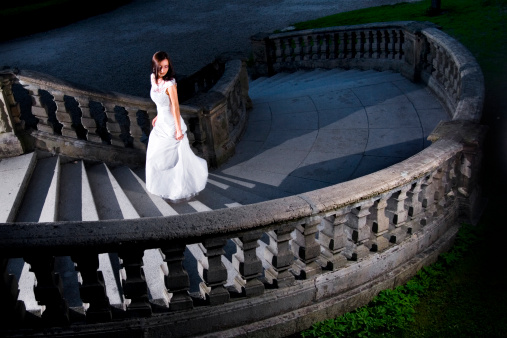 Young classy woman in white dress climbing the palace stairs.