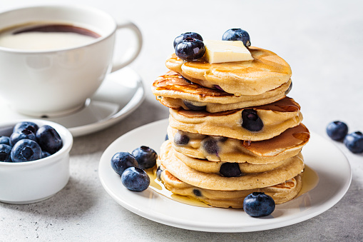 Stack of blueberry pancakes with maple syrup and butter on a white breakfast plate.