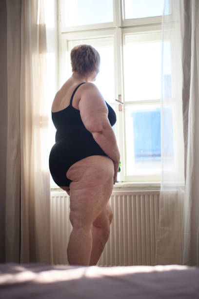 孤独な太った女性が立って、自宅の窓から見ているの背面図。 - mature adult sadness overweight women ストックフォトと画像