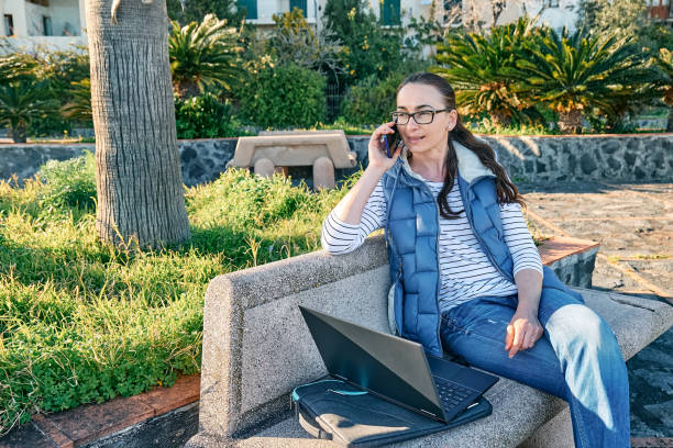 istock Sporty woman wearing eyeglasses with laptop computer working outdoors, talking on phone while sitting on bench at the seaside. Modern lifestyle, connection, blogging, business, freelance concept. 1373143696