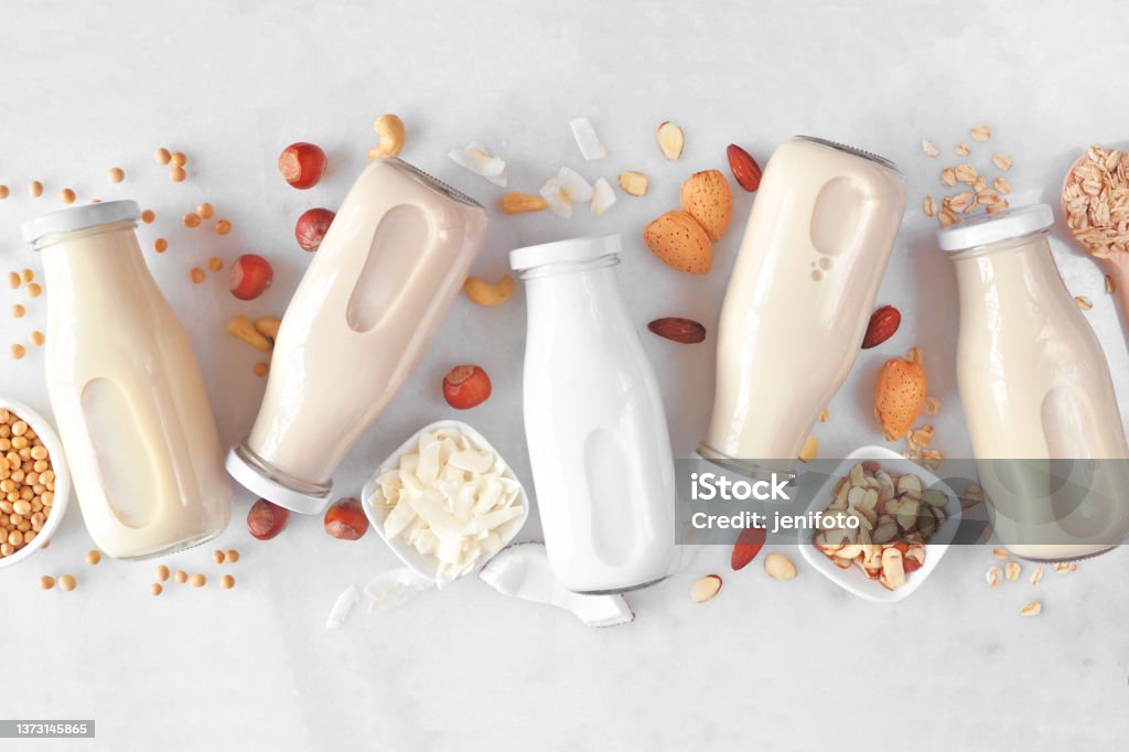 Vegan, plant based, non dairy milk milk bottles with scattered ingredients over white marble Vegan, plant based, non dairy milk. Variety in milk bottles with scattered ingredients. Above view over a white marble background. Almond Milk Stock Photo