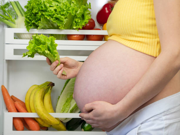Pregnant woman takes lettuce from the fridge, woman opens the fridge and holds a salad leaf in her hand. fresh fruit and vegetables food stock photo