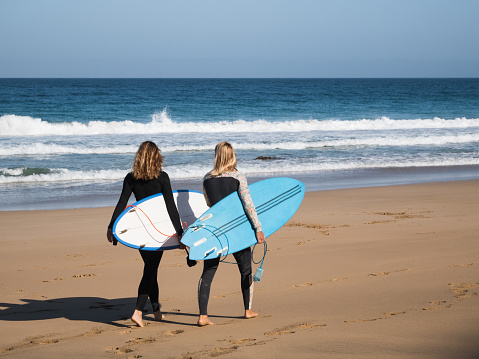 Unrecognizable surfer women walking by the beach shore watching the waves