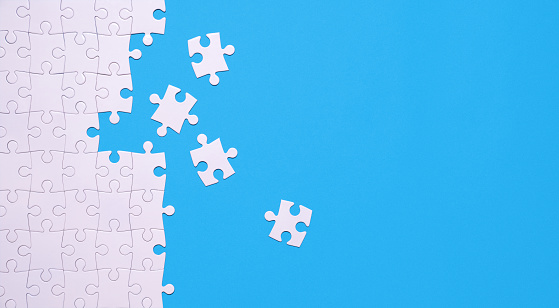 Unfinished white jigsaw puzzle isolated on blue background with copy space