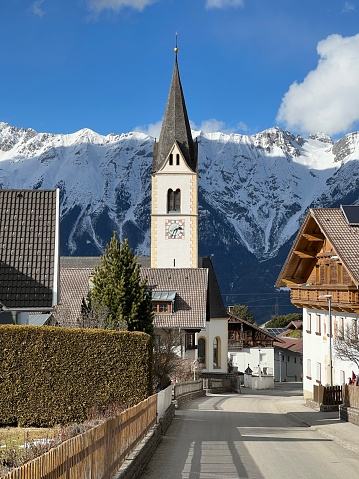 town sistrans with church in tirol austria.. streetview with tree, fence and nordkette mountains in the background