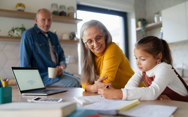 Small girl with senior grandparents doing maths homework at home. A small girl with senior grandparents doing maths homework at home. human relationship stock pictures, royalty-free photos & images