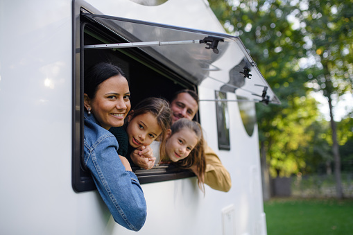 A happy young family with two children looking out of caravan window.