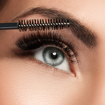 Close-up of female face and mascara wand for maximum volume of artificial eyelashes