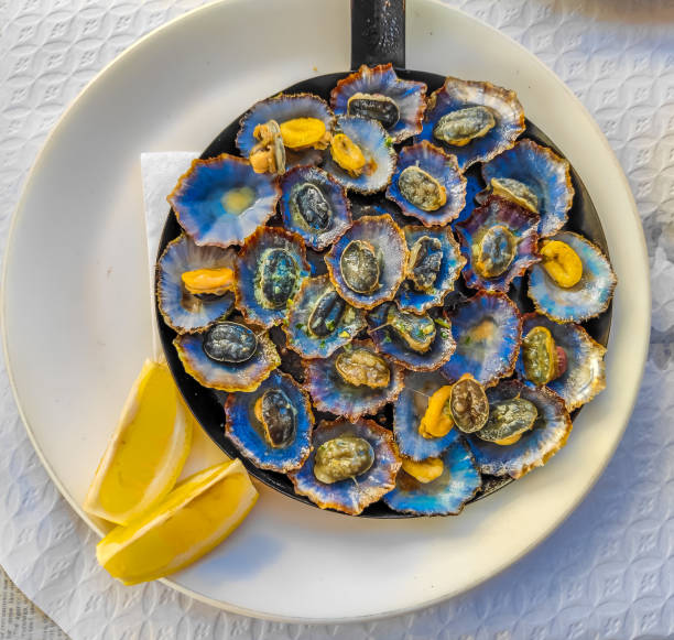 Cooked limpets served in a cast iron with a lemon slices Cooked limpets served in a cast iron with a lemon slices in a restaurant in Madeira island madeira sauce stock pictures, royalty-free photos & images