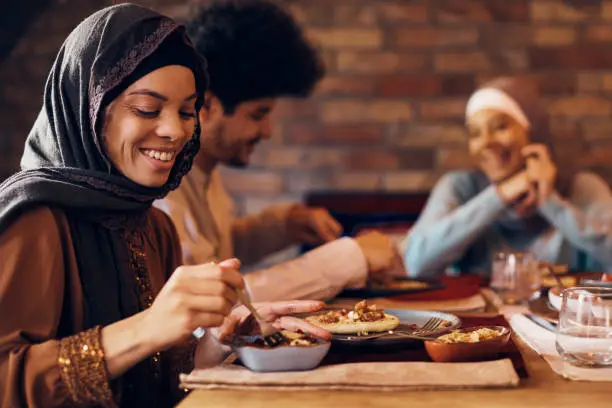 Happy Middle Eastern woman having Ramadan Iftar meal with her family at dining table.