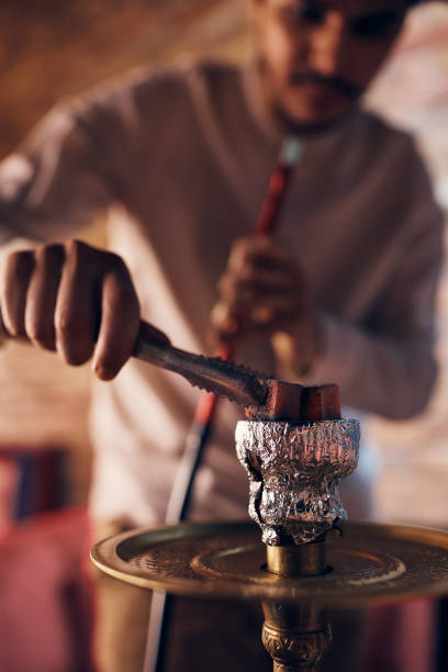 istock Close-up of Arabian man adding hot coal while smoking hookah. 1373158499