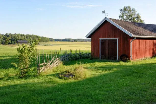 Photo of Traditional Finnish red wooden barn with roundpole fence