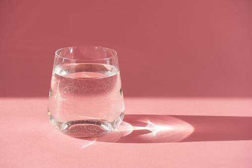 Glass of fresh clear water on a pink background. Horizontal orientation.