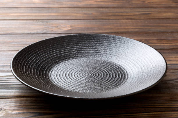 istock Perspective view of empty black plate on wooden background. Empty space for your design 1373171086