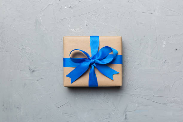 istock Holiday gift box wrapped in craft paper with colored bow on table background. Top view, flat lay, copy space 1373171114