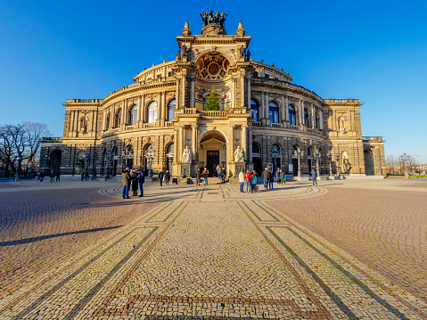 Dresden, Germany - January 01, 2020: Theaterplatz in Dresden with Semperoper opera building. The Theaterplatz is an open place for demonstrations and tourists. A meeting point with Semperoper, Hofkirche, Zwinger and Hausmannsturm around. Tourists are walking around and taking photos.