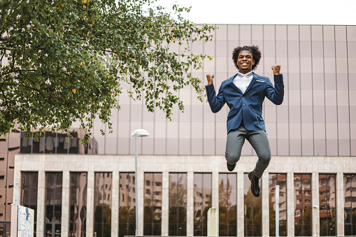 An African American excited businessman jumping with hands in fist