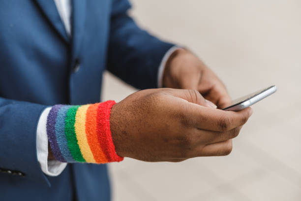 close-up of dark skinned hands with smartphone and lgbt bracelet outdoors . lgbtqia culture. - homosexual gay pride business rainbow imagens e fotografias de stock