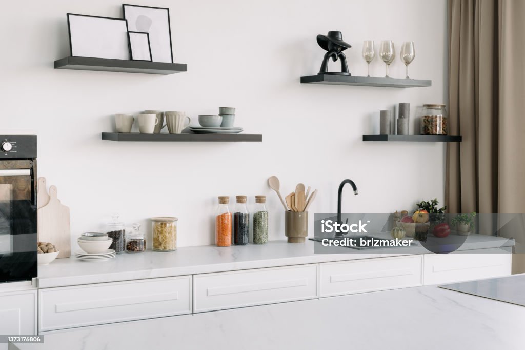 Modern kitchen in whine tones with appliances and decor Contemporary kitchen interior design with white furniture, appliances, decor and black sink. Bright and spacious dining room. Luxury apartment. Cooking time Kitchen Counter Stock Photo