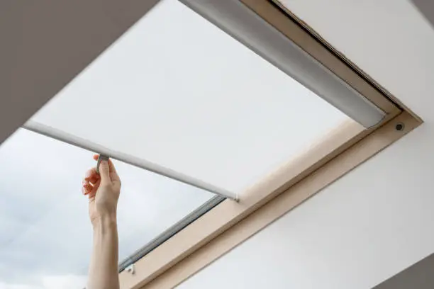 Photo of Woman hand open blinds on attic or mansard window