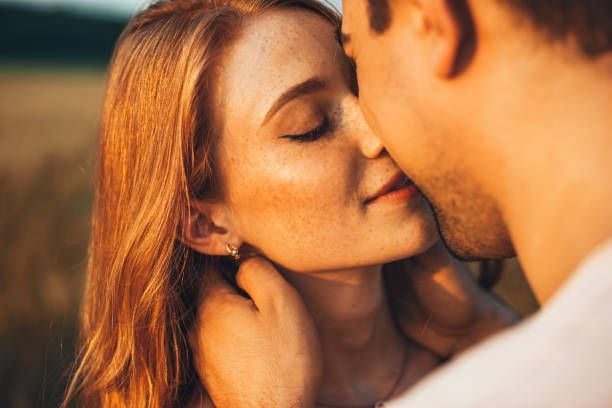 Close-up portrait of a freckled girl kissing her boyfriend while they are on an outdoor date. Wheat field. People lifestyle concept. stock photo