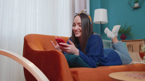 istock Cheerful young woman lying on sofa, using mobile phone share messages on social media application 1373187753