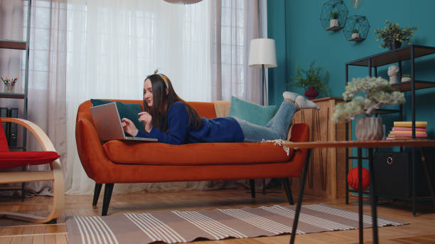 istock Cheerful young woman lying on sofa, using laptop pc share messages on social media application 1373187853