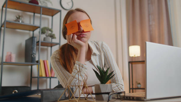 Tired woman teacher using laptop computer with funny stickers on eyes sleeps at workplace, napping